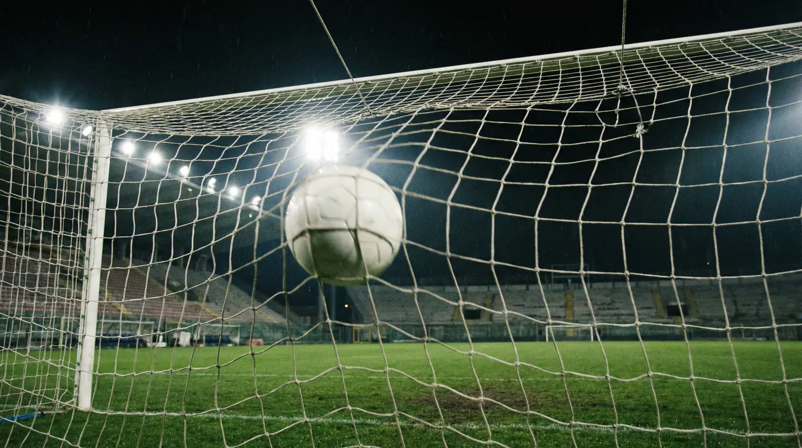 Balón de fútbol entrando en la red de una portería de un estadio italiano iluminado